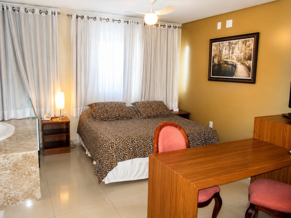 Quarto com cama de casal, mesa de madeira e banheira de hidromassagem em mármore